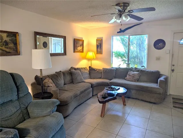 Living room with ceiling fan, a textured ceiling, and light tile patterned flooring
