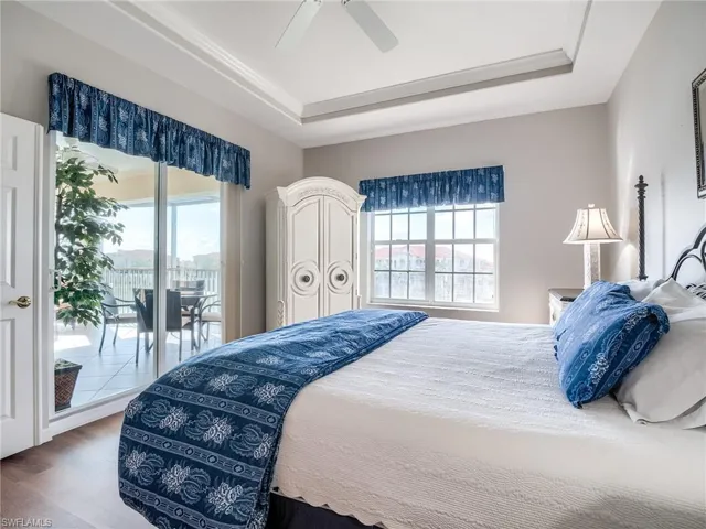 Bedroom featuring a raised ceiling, access to exterior, ceiling fan, and wood finished floors