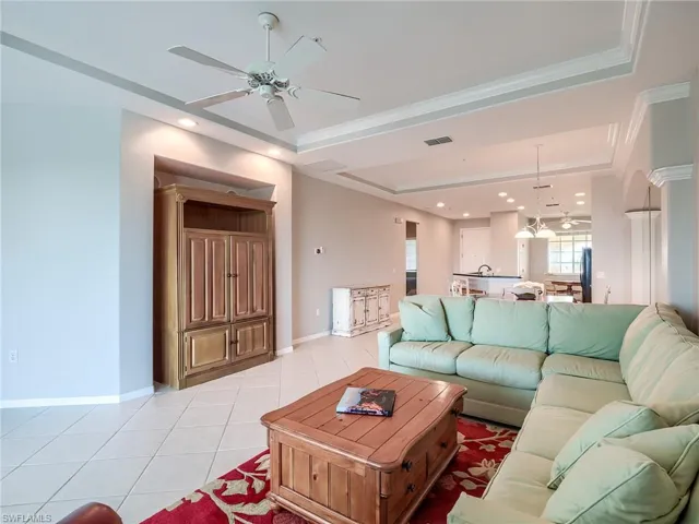 Living room with light tile patterned flooring, a ceiling fan, recessed lighting, a raised ceiling, and ornamental molding