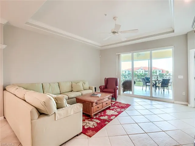Living area featuring a raised ceiling, light tile patterned floors, a ceiling fan, and crown molding