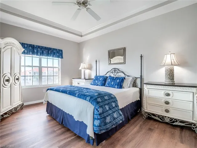 Bedroom featuring dark wood finished floors, a ceiling fan, a tray ceiling, and crown molding