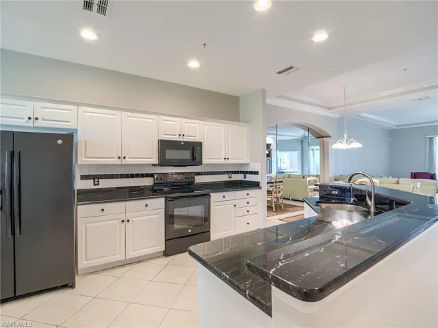 Kitchen featuring black appliances, decorative backsplash, white cabinets, arched walkways, and light tile patterned flooring