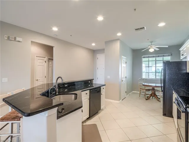 Kitchen featuring a kitchen island with sink, white cabinets, recessed lighting, a kitchen bar, and light tile patterned floors