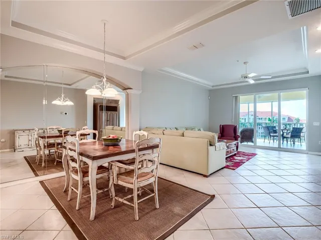Dining room featuring a tray ceiling, light tile patterned floors, ceiling fan, crown molding, and arched walkways