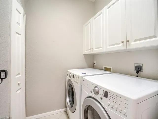 Washroom with washer and dryer, a textured wall, cabinet space, and light tile patterned floors