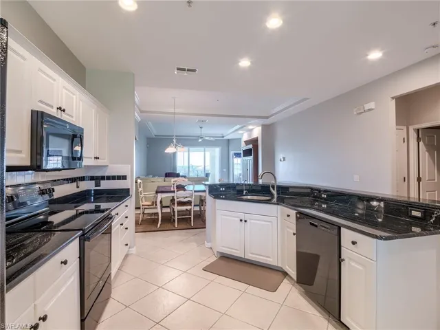 Kitchen featuring black appliances, white cabinets, dark stone countertops, decorative light fixtures, and light tile patterned flooring