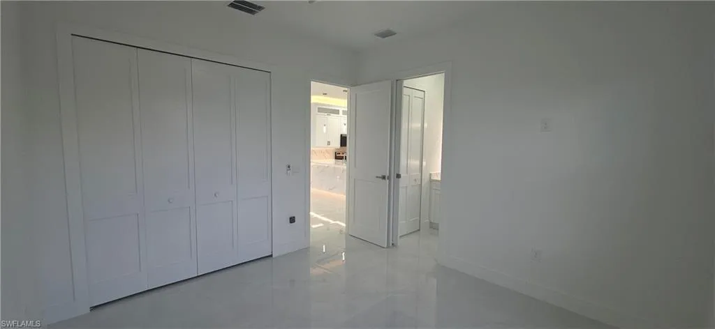 White bi-fold closet doors with panel detailing, glossy tile flooring, and white painted walls