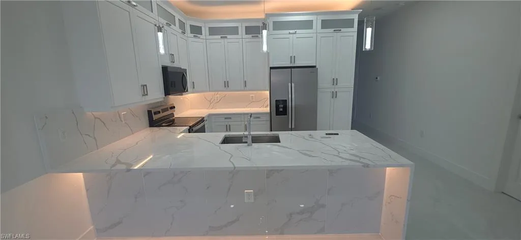 Kitchen featuring a large central island with undermount sink, white cabinetry with upper glass-front accents, stainless steel appliances, and integrated under-cabinet lighting