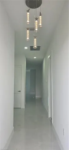 Contemporary hallway featuring a multi-light pendant fixture, recessed lighting, and light-toned tile flooring