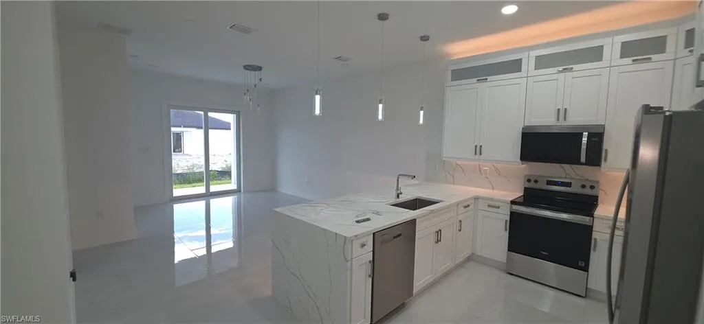 Modern kitchen featuring white cabinetry, quartz countertops, a stainless steel appliance suite, and contemporary pendant lighting