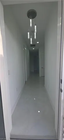 Long hallway featuring a contemporary multi-pendant light fixture, recessed lighting, white walls, white baseboards, and light-colored tile flooring