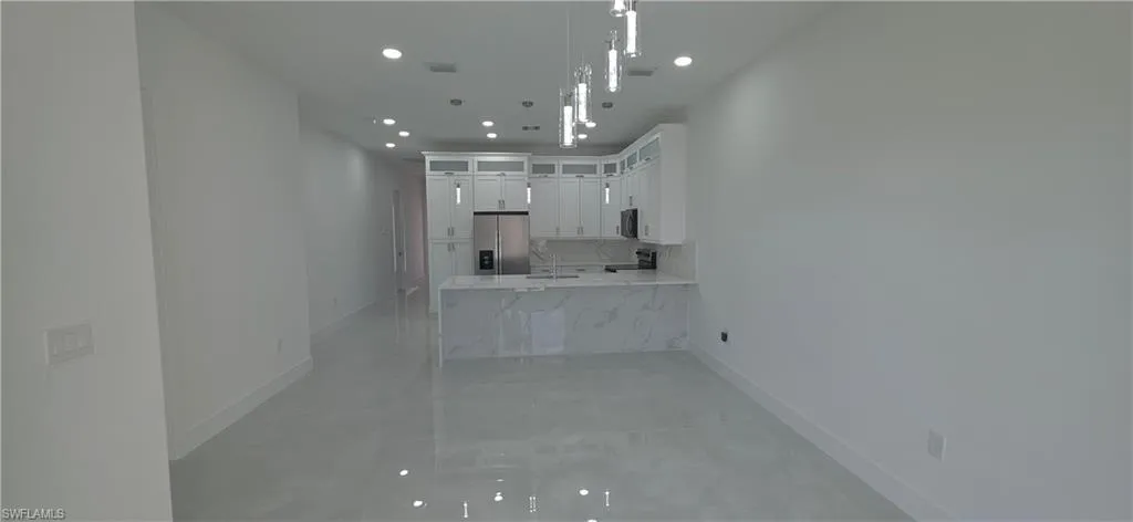 Modern kitchen featuring white cabinetry, a stainless steel refrigerator, and a light-toned countertop with a waterfall edge