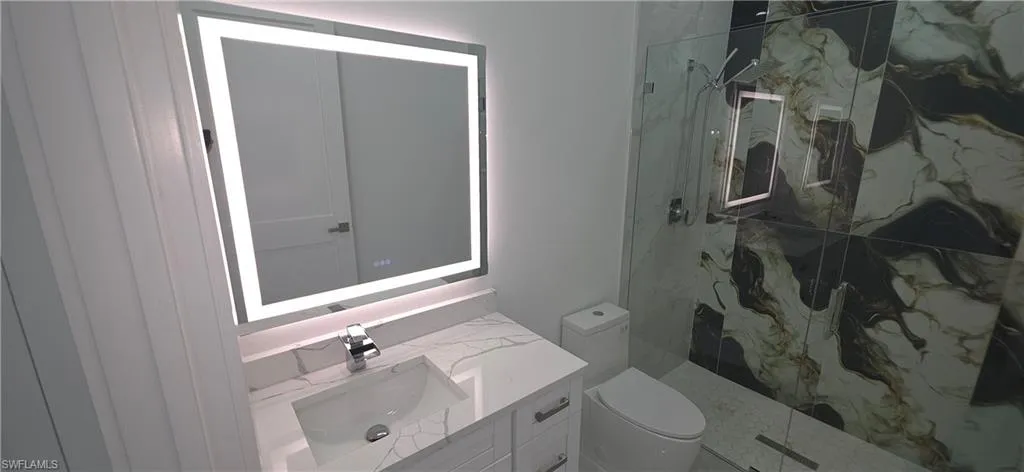 Bathroom featuring a contemporary vanity with a white countertop and integrated sink, an illuminated mirror, and a glass-enclosed shower with large format marble-look tile