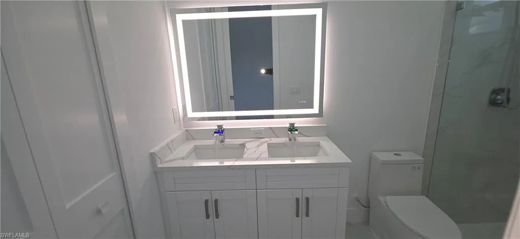 Dual vanity with stone-finish countertop, integrated sinks, and backlit mirror