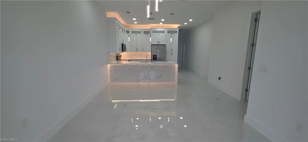 Open-concept kitchen and living area featuring sleek white cabinetry, a waterfall-edge island with integrated lighting, stainless steel appliances, and glossy tile flooring throughout