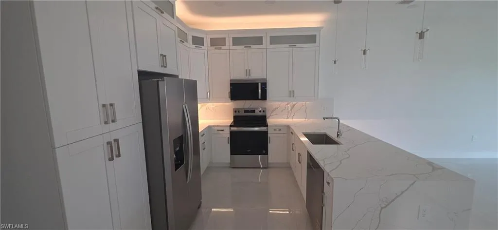 Contemporary kitchen featuring a stainless steel French door refrigerator, white shaker-style cabinetry, and a U-shaped countertop with a waterfall edge