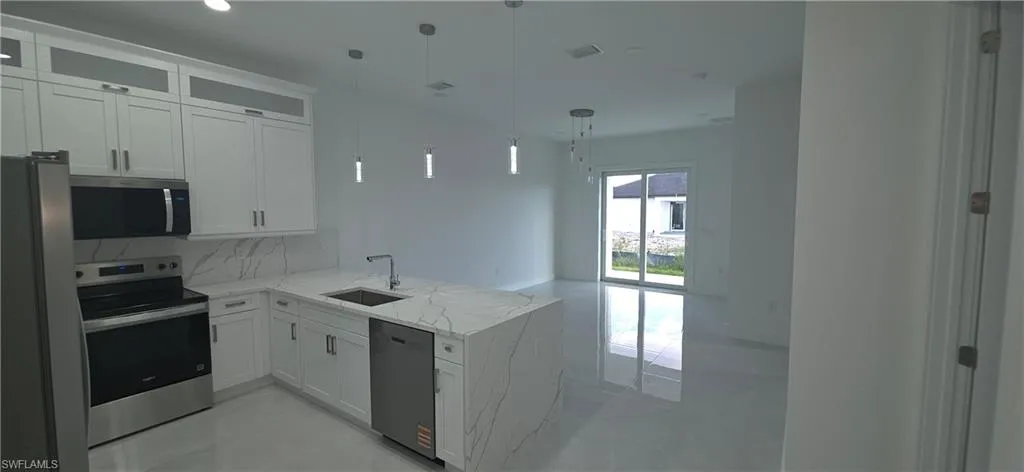 Modern kitchen featuring a waterfall-edge island with integrated sink, white cabinetry with upper glass accents, stainless steel appliances, and large format tile flooring