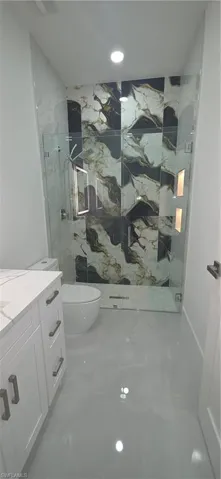 Contemporary bathroom featuring a spacious glass-enclosed shower with black and white patterned tile, integrated shower niches with lighting, a modern commode, and a white vanity with a light-toned countertop