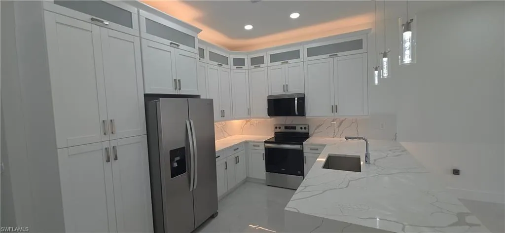 Kitchen featuring white shaker cabinetry, an integrated stainless steel sink, under-cabinet lighting, and a countertop with subtle veining