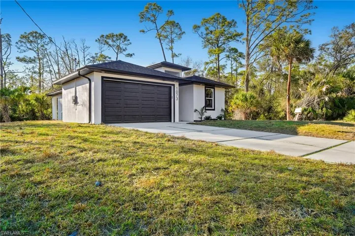 View of front of house featuring stucco siding, concrete driveway, a front lawn, and a garage