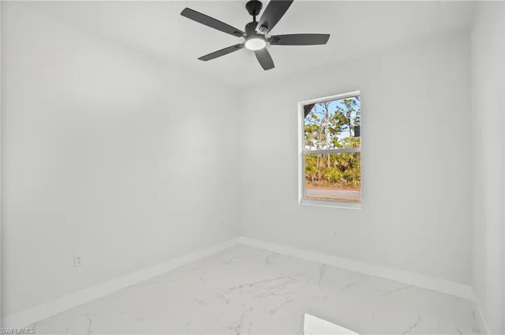 Empty room featuring marble look tiles and a ceiling fan