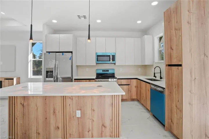 Dual tone kitchen with a center island, modern cabinets, stainless steel appliances, two tone cabinetry, and decorative light fixtures