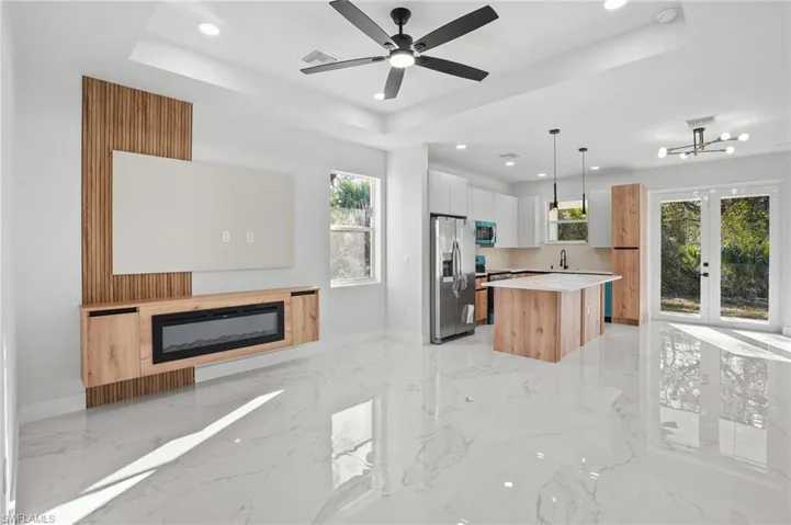 Dual tone kitchen with two tone cabinetry, a kitchen island, a glass covered fireplace, stainless steel appliances, and light marble finish floors