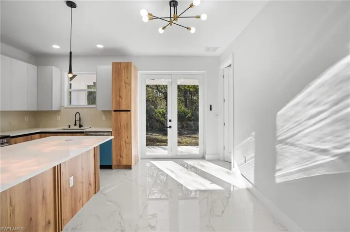 Kitchen featuring dual tone cabinets, modern cabinets, french doors, light stone countertops, and suspended lighting