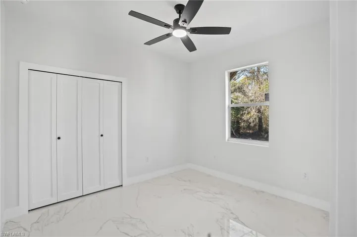 Unfurnished bedroom featuring light marble finish floors, a ceiling fan, and a closet