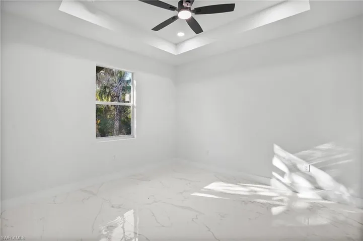 Empty room with a raised ceiling, ceiling fan, recessed lighting, and marble finish flooring