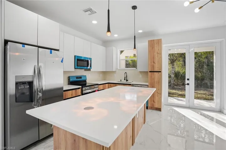 Kitchen featuring stainless steel appliances, a kitchen island, decorative light fixtures, light marble finish flooring, and modern cabinets