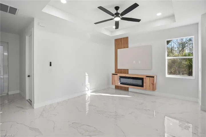 Unfurnished living room with a glass covered fireplace, recessed lighting, a ceiling fan, a tray ceiling, and light marble finish flooring
