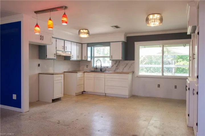 Kitchen with a sink, visible vents, under cabinet range hood, decorative backsplash, and white cabinets