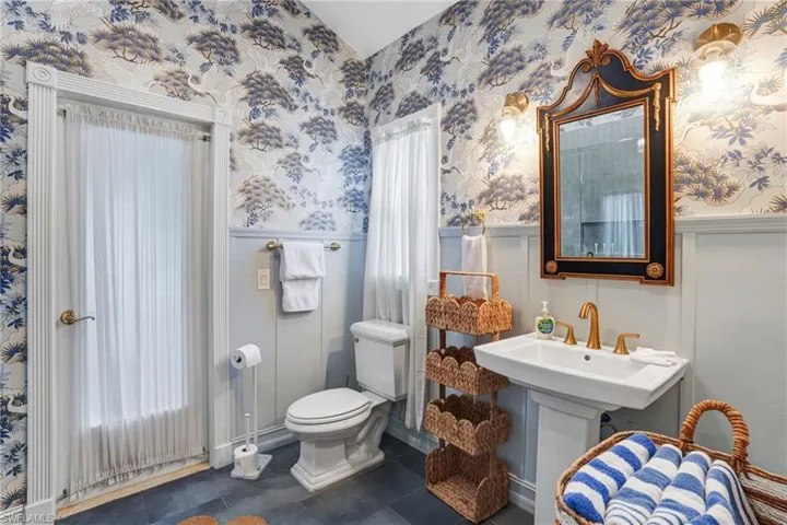 Half bathroom with wallpapered walls, a wainscoted wall, and dark tile patterned floors - Virtually Edited Image