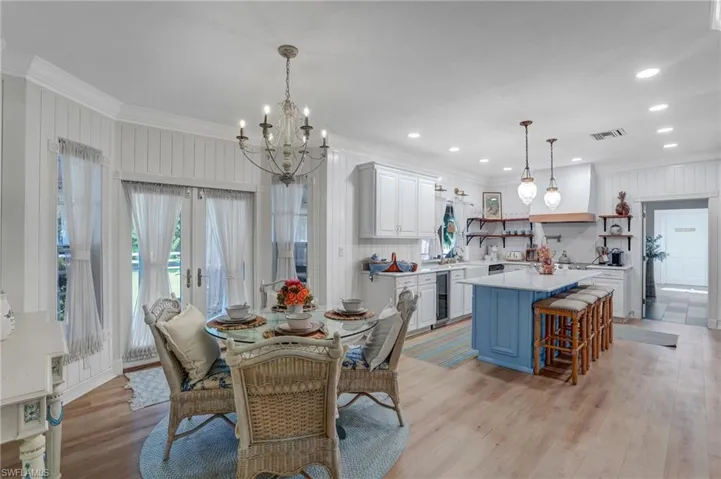 Dining room featuring ornamental molding, light wood-style flooring, a chandelier, beverage cooler, and french doors - Virtually Edited Image