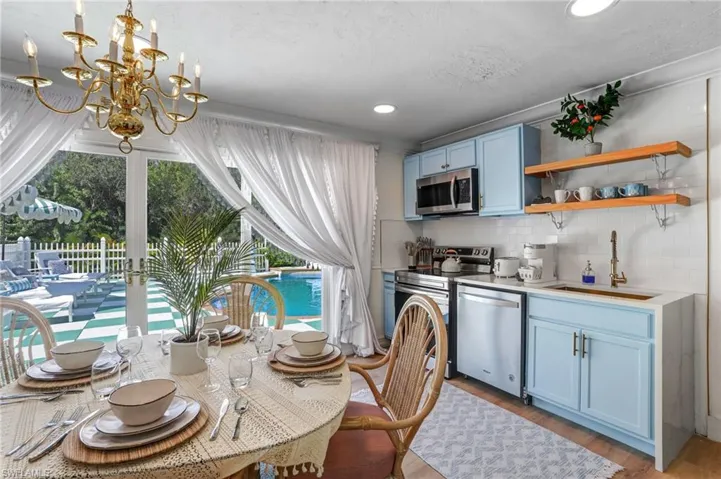 Kitchen featuring blue cabinetry, open shelves, stainless steel appliances, tasteful backsplash, and light wood-style floors - Virtually Edited Image