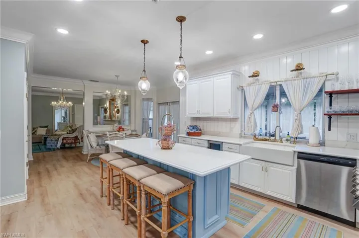 Kitchen featuring white cabinets, stainless steel dishwasher, a center island, ornamental molding, and light wood-type flooring - Virtually Edited Image