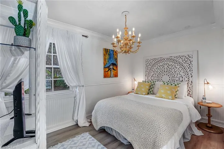 Bedroom with wood finished floors, a chandelier, a wainscoted wall, and ornamental molding - Virtually Edited Image
