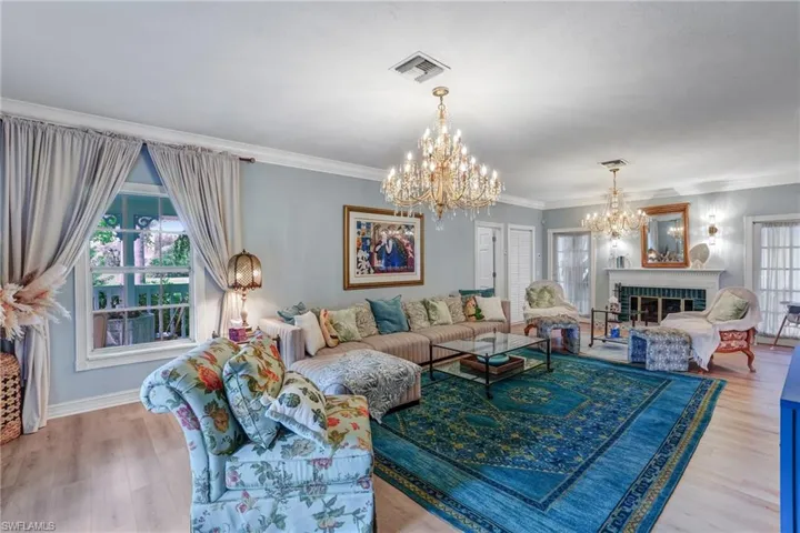 Living area featuring a brick fireplace, ornamental molding, wood finished floors, and a chandelier - Virtually Edited Image
