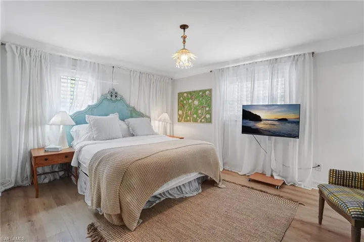 Bedroom featuring multiple windows, light wood finished floors, and ornamental molding - Virtually Edited Image