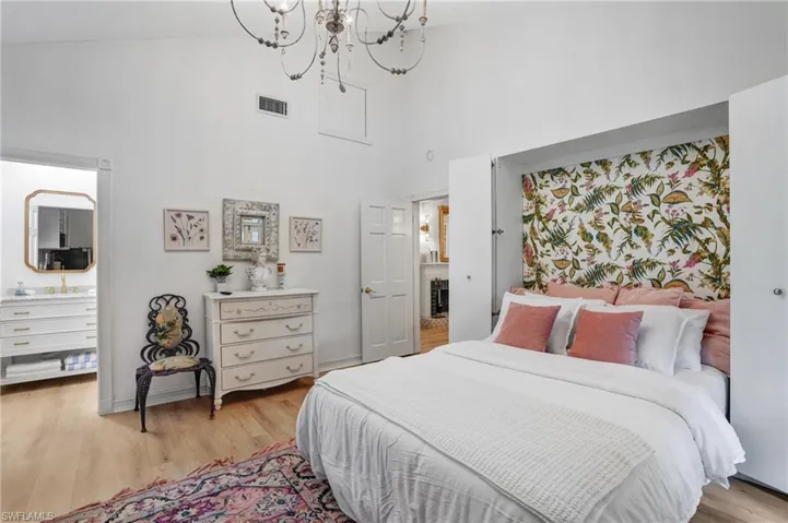 Bedroom with high vaulted ceiling, light wood finished floors, and a chandelier - Virtually Edited Image