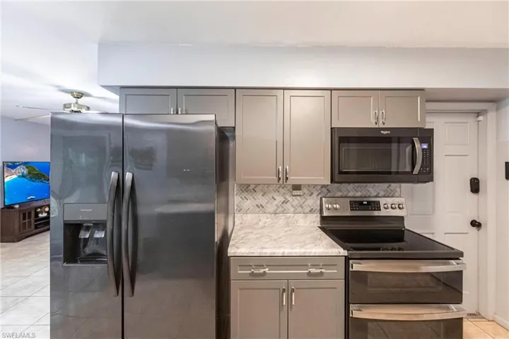 Kitchen featuring appliances with stainless steel finishes, decorative backsplash, gray cabinetry, ceiling fan, and light tile patterned flooring