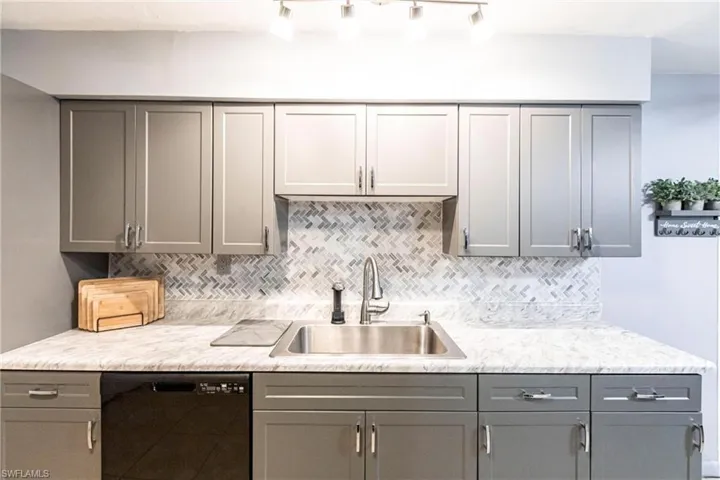 Kitchen with decorative backsplash, sink, black dishwasher, and gray cabinets