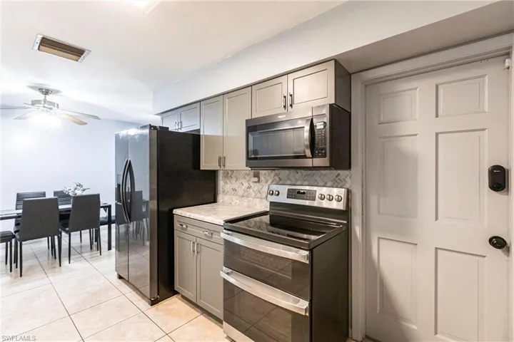 Kitchen with light tile patterned flooring, backsplash, gray cabinetry, and stainless steel appliances