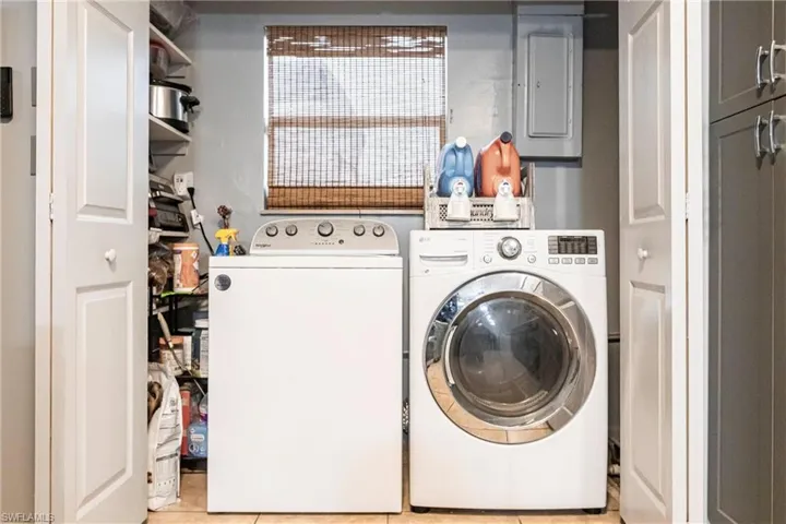 Laundry room with electric panel, independent washer and dryer, and light tile patterned flooring