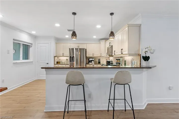 Kitchen with stainless steel appliances, backsplash, kitchen peninsula, dark stone counters, and decorative light fixtures
