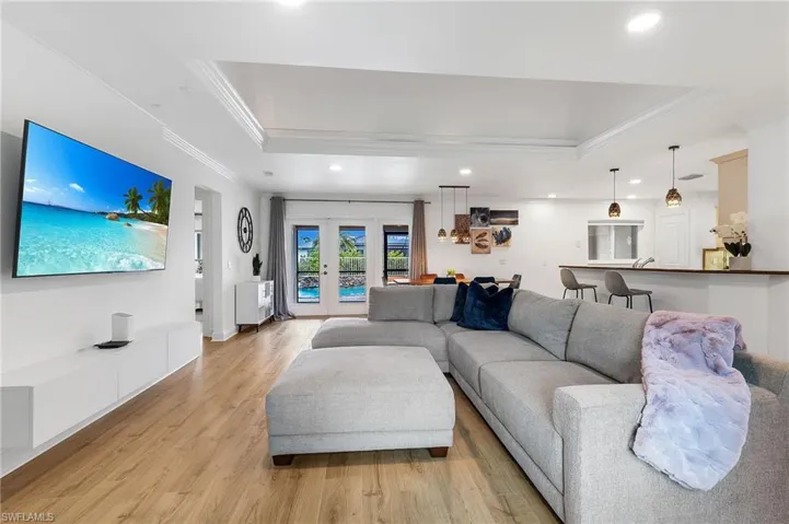 Living room with a raised ceiling, ornamental molding, and light wood-type flooring