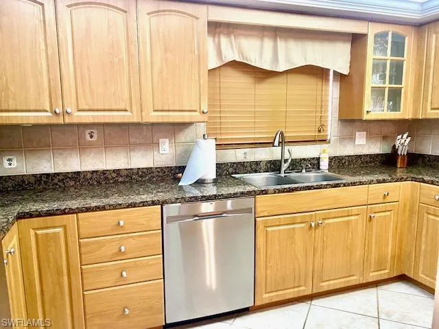 Kitchen featuring a sink, dishwasher, light tile patterned floors, backsplash, and glass insert cabinets