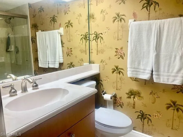 Full bath featuring vanity, wallpapered walls, a shower stall, and toilet