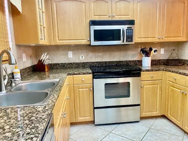 Kitchen with appliances with stainless steel finishes, light brown cabinetry, tasteful backsplash, a sink, and light tile patterned floors